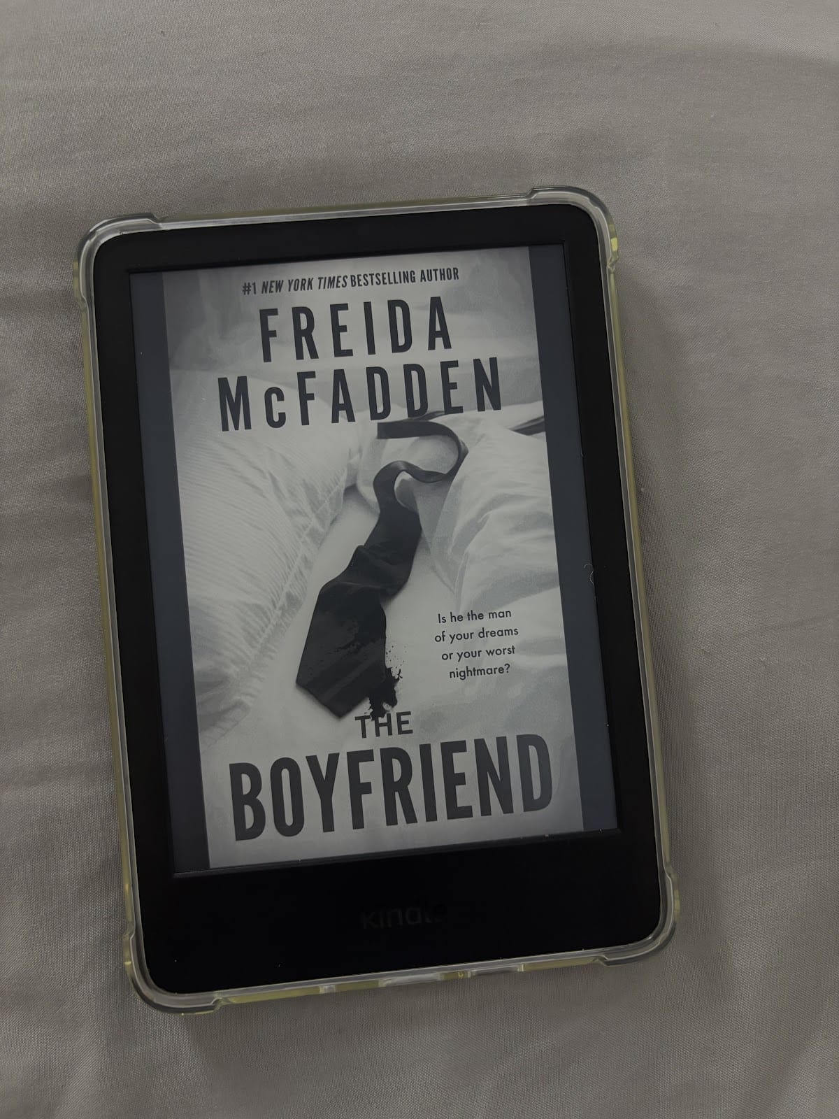 Un lector electrónico Kindle que muestra la portada del libro "The Boyfriend", de Freida McFadden. La portada muestra una corbata negra sobre una colcha blanca, con un texto que dice: "¿Es el hombre de tus sueños o tu peor pesadilla?