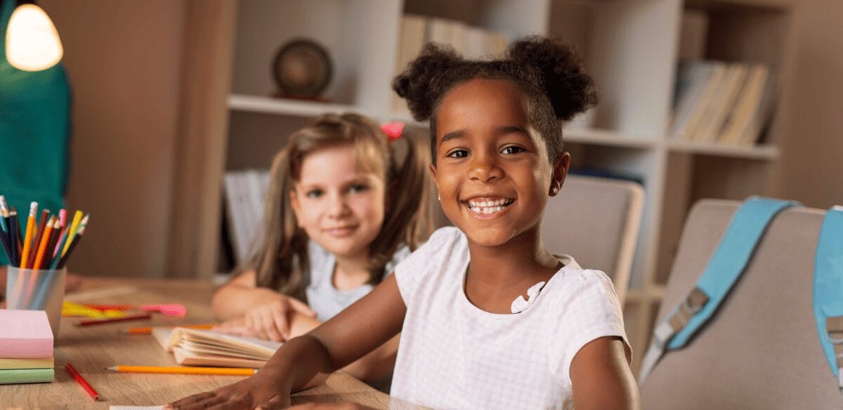 Dos niños sentados a una mesa, con las manos apoyadas en el escritorio, realizando juntos una actividad concentrada.