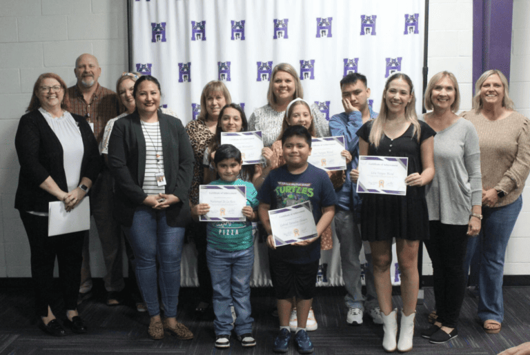 Un grupo diverso de personas exhibe con orgullo sus certificados ante una vibrante pared morada.