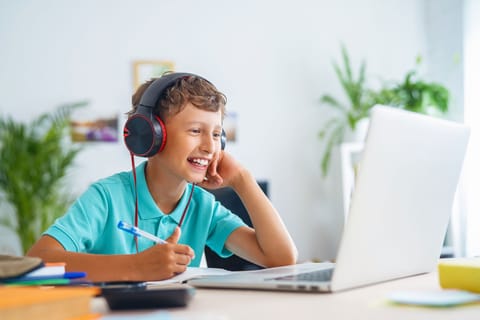 Un chico con auriculares está sentado en un escritorio, concentrado en su portátil, inmerso en su trabajo o entretenimiento.