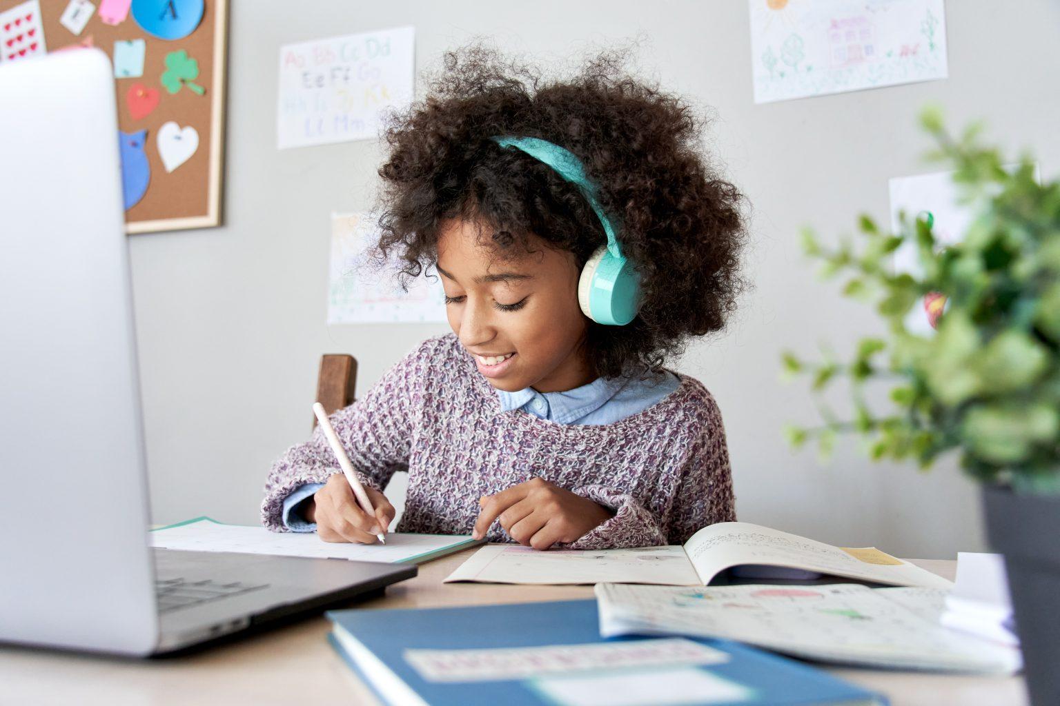 Una joven con auriculares se concentra en escribir sentada frente a un ordenador portátil.